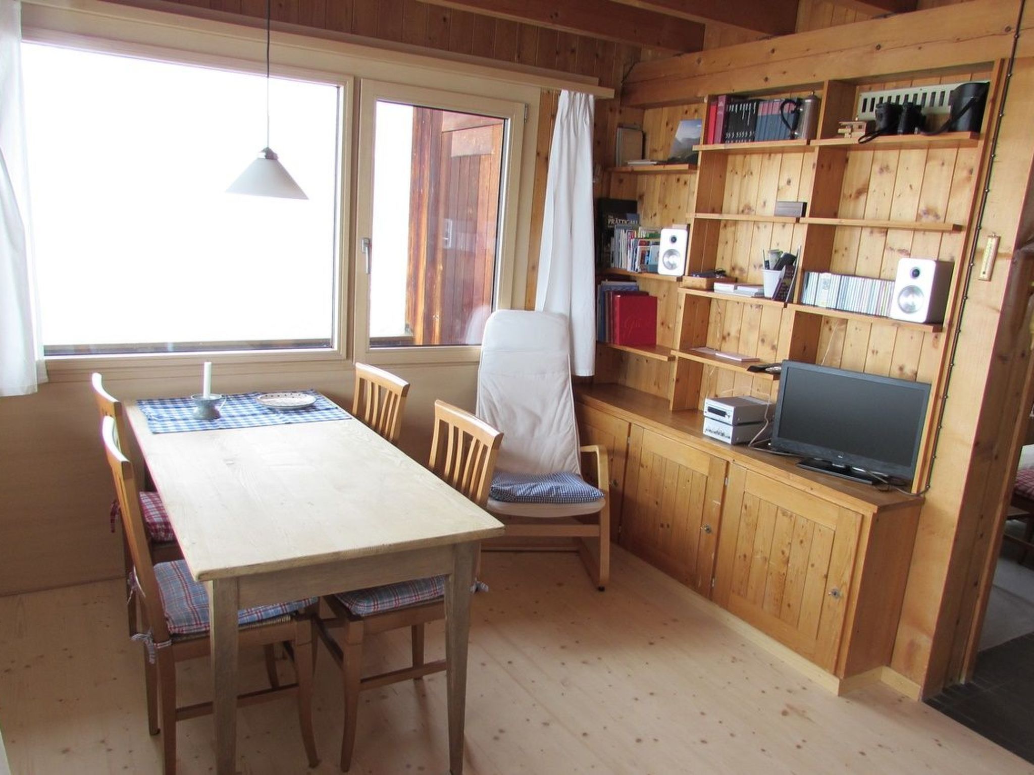 Un interior de madera con una mesa de comedor, sillas, un televisor y estanterías con libros y objetos.