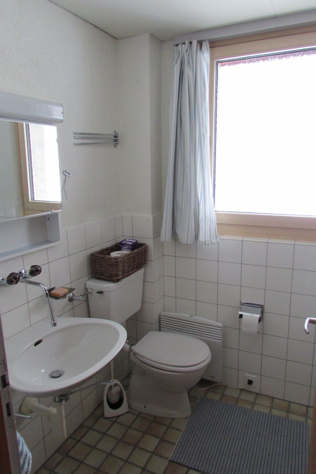 Ein kleines Badezimmer mit Toilette, Waschbecken und einem Fenster mit Vorhang.