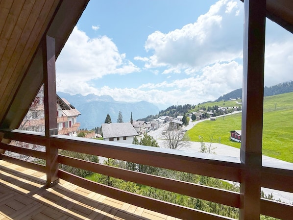 A wooden balcony with a view of a village and mountains.