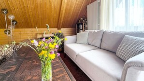 A cozy loft bedroom with a wooden ceiling, a sofa, a coffee table with a vase of flowers, and a bookshelf. - Haus DOMO, (Flumserberg Tannenboden), by Interhome (Mols)