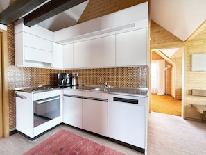 Cocina compacta con gabinetes blancos, horno empotrado, cafetera y salpicadero de azulejos.