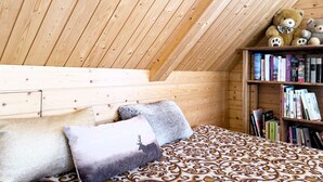 A cozy attic bedroom with a sloped wooden ceiling, a bed with patterned bedding, a bookshelf, and a teddy bear. - Haus DOMO, (Flumserberg Tannenboden), by Interhome (Mols)