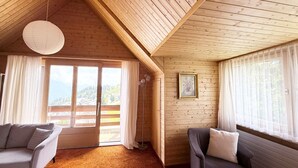 A cozy room with a sloped ceiling, two sofas, a large window with curtains, and a view of a mountainous landscape. - Haus DOMO, (Flumserberg Tannenboden), by Interhome (Mols)