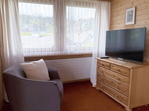 Una habitación con un sofá, un televisor sobre un mueble de madera y una ventana con cortinas.