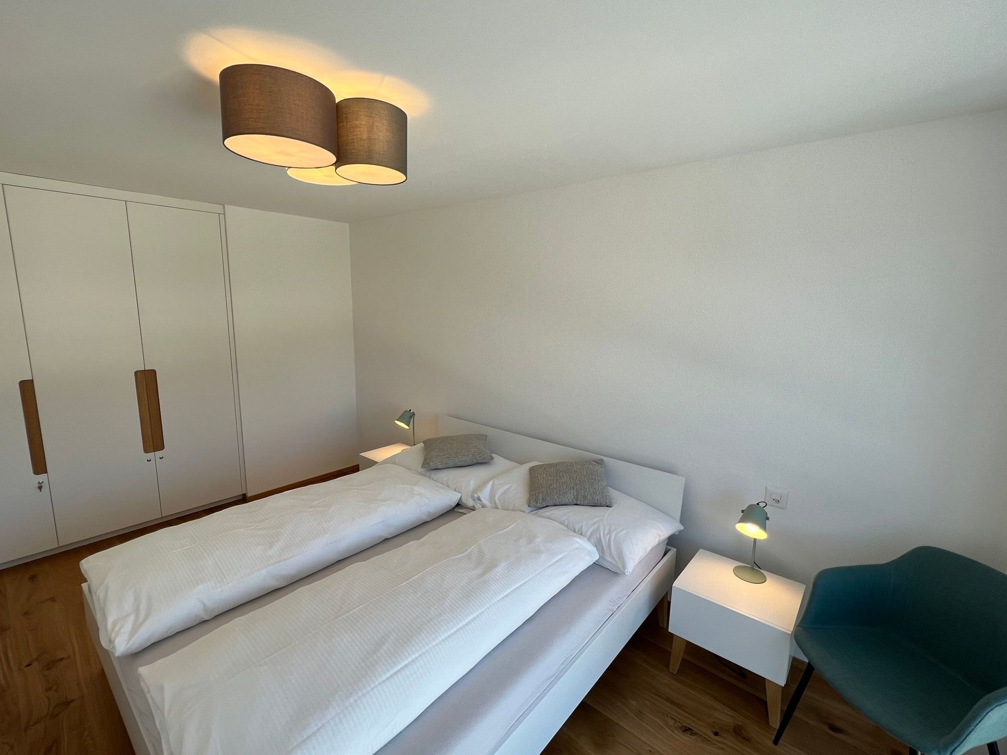 A bedroom with a bed, bedside tables, a chair, and a wardrobe.