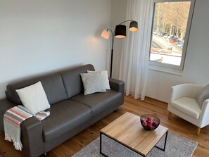 A modern living room with a grey sofa, a white armchair, a coffee table with a bowl of apples, and a floor lamp.
