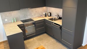 Een moderne keuken met donkere kastjes, een inbouwoven, een spoelbak en een aanrecht met waterkoker en kopjes.