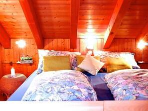 A wooden cabin bedroom with a bed, pillows, a nightstand, and a wall-mounted shelf.