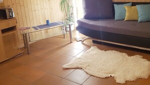 Et hyggeligt værelse med en sofa, et glasbord, et træskab og en blød, hvid måtte.