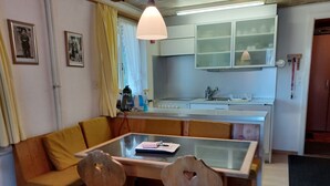Ett kompakt kök med en matplats, med ett bord med glasskiva, trästolar och en gul soffa.