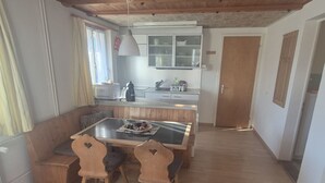 En matplats med ett träbord och stolar, ett kök i bakgrunden och ett träpanelat tak.