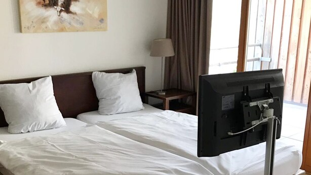 Una habitación de hotel con cama, televisor, lámpara y un cuadro en la pared.
