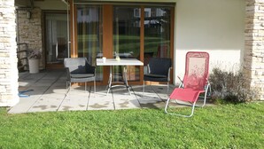Un patio con mesa y sillas, una puerta corredera de vidrio y un muro de piedra.