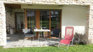 Une terrasse avec une table et des chaises, une porte-fenêtre coulissante et un mur en pierre.