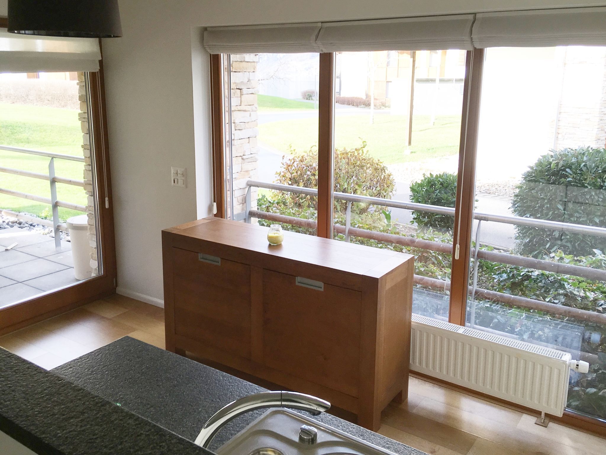 Une cuisine avec des meubles de rangement en bois, une fenêtre donnant sur un jardin et un radiateur.