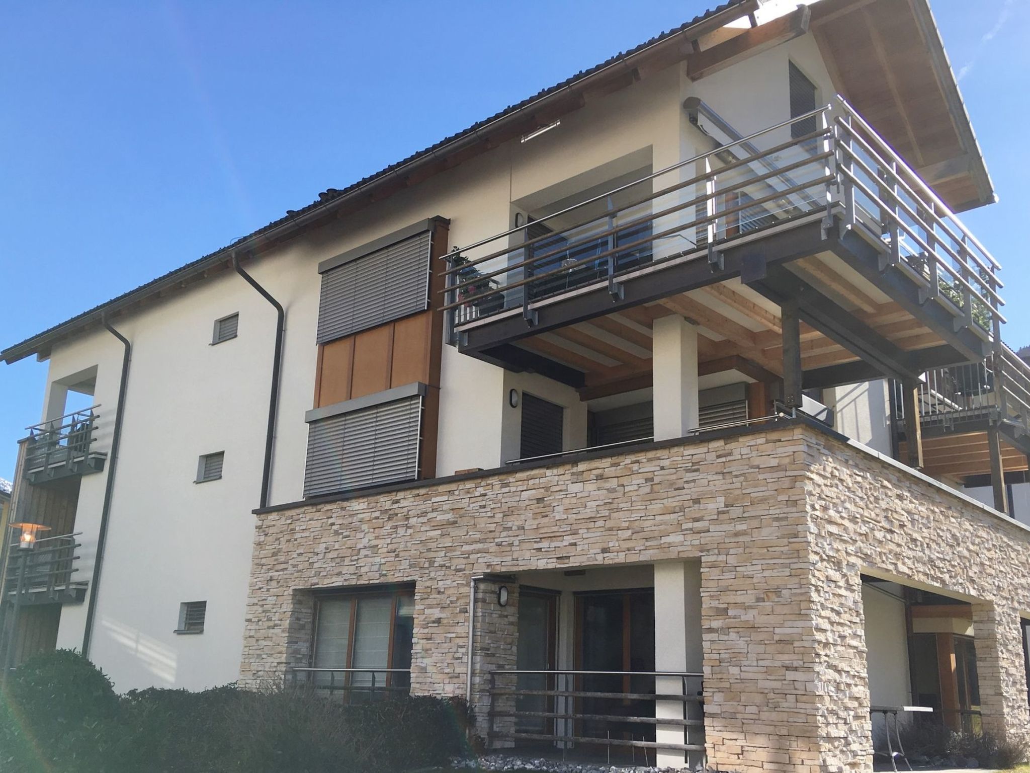 A modern two-story house with a stone facade, a balcony, and a flat roof.