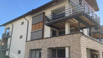 A modern two-story house with a stone facade, a balcony, and a flat roof.