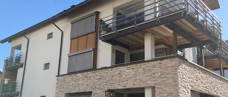 A modern two-story house with a stone facade, a balcony, and a flat roof.