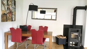 Un comedor con una mesa de madera y sillas rojas, una lámpara negra, un espejo y un estufa de leña.