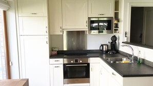 Una cocina moderna con armarios blancos, un horno Bosch, microondas y cafetera.