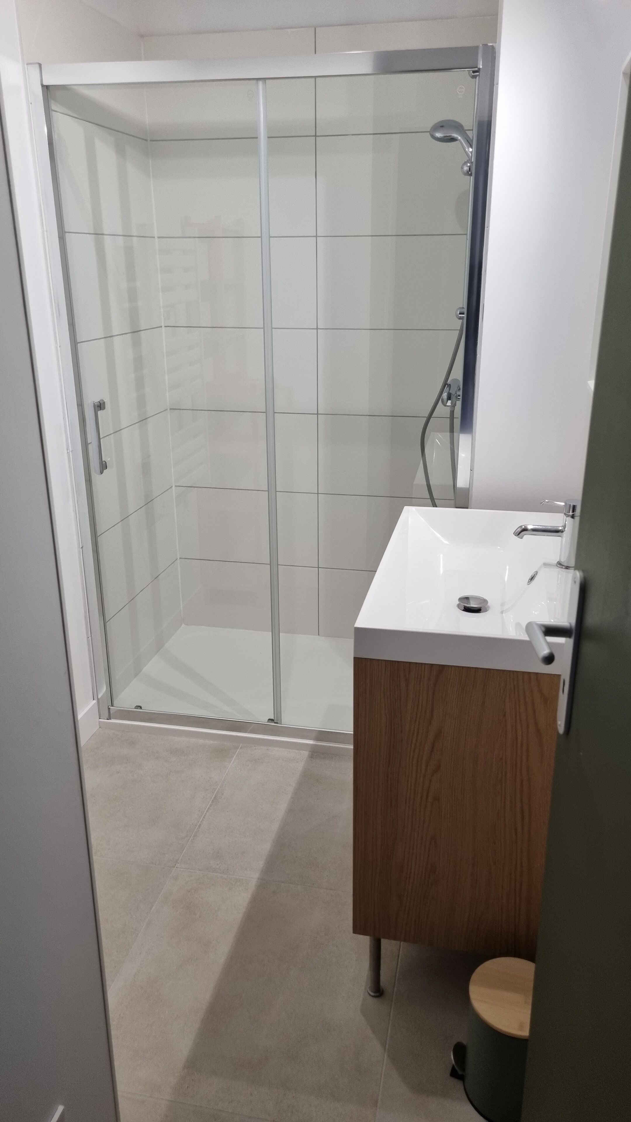 Une salle de bain avec une douche à parois de verre, un lavabo blanc et un meuble-lavabo en bois.