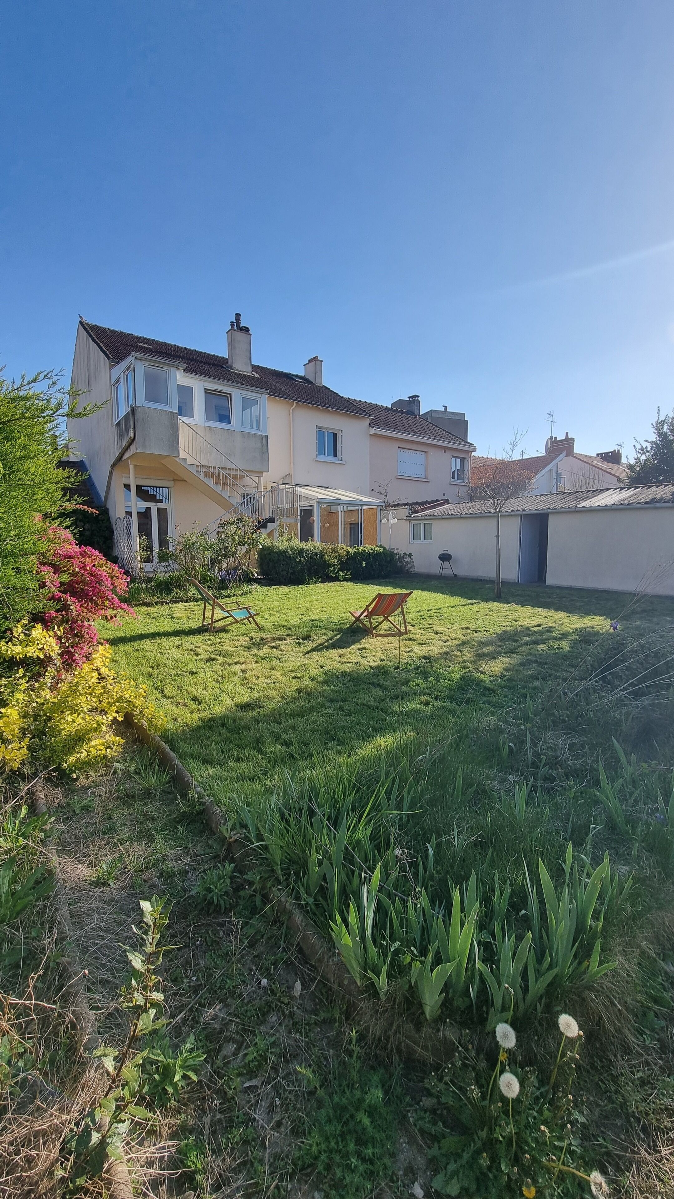 Une maison à deux étages dotée d’un patio couvert, d’un petit jardin avec une pelouse et d’un arbre.