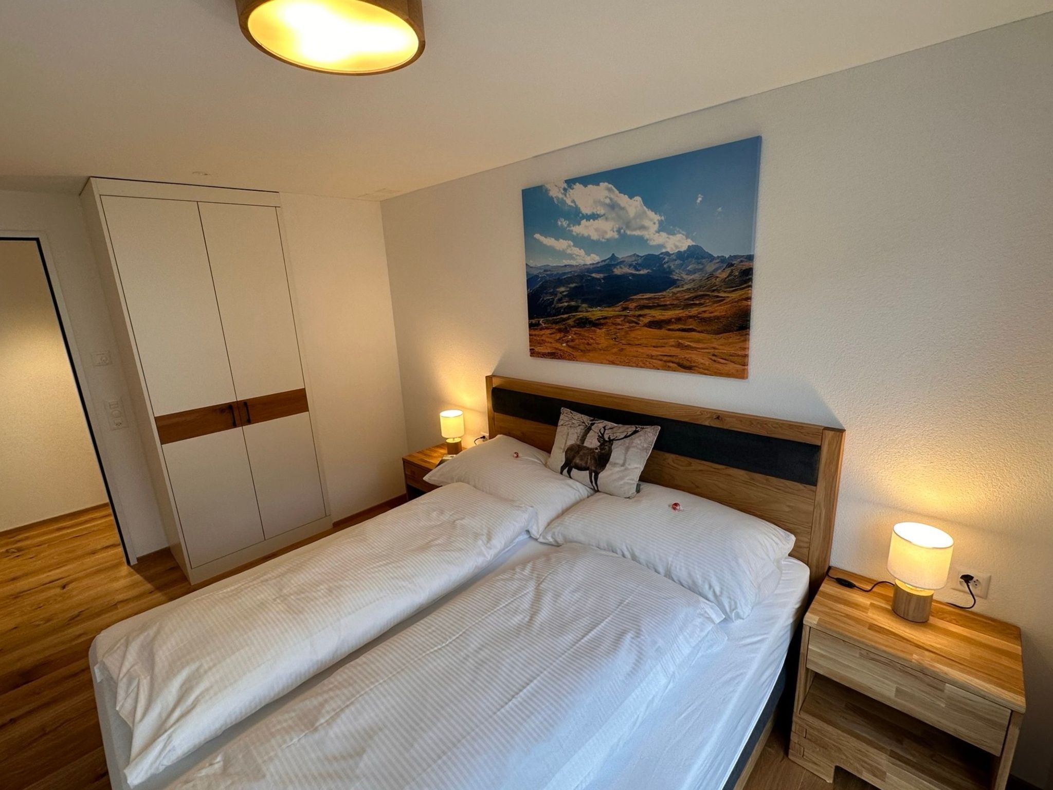 Ein Schlafzimmer mit Bett, Nachttisch, Lampe, Schrank und einem Bild an der Wand.