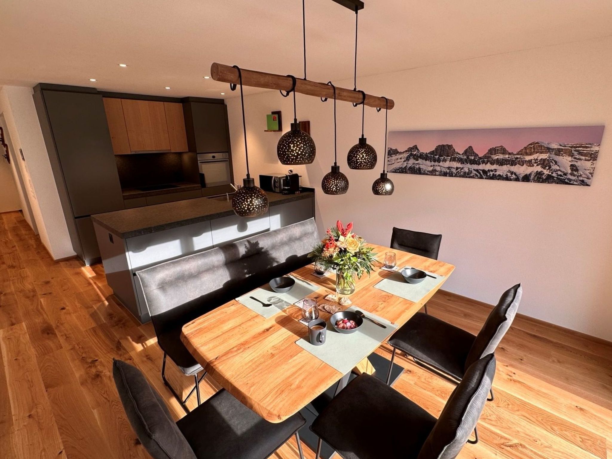 Eine moderne Küche mit Essbereich, Holzboden und Pendelleuchten.