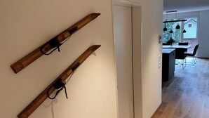 A hallway with wooden skis mounted on the wall, a white door, and a view into a dining area with a table and chairs.