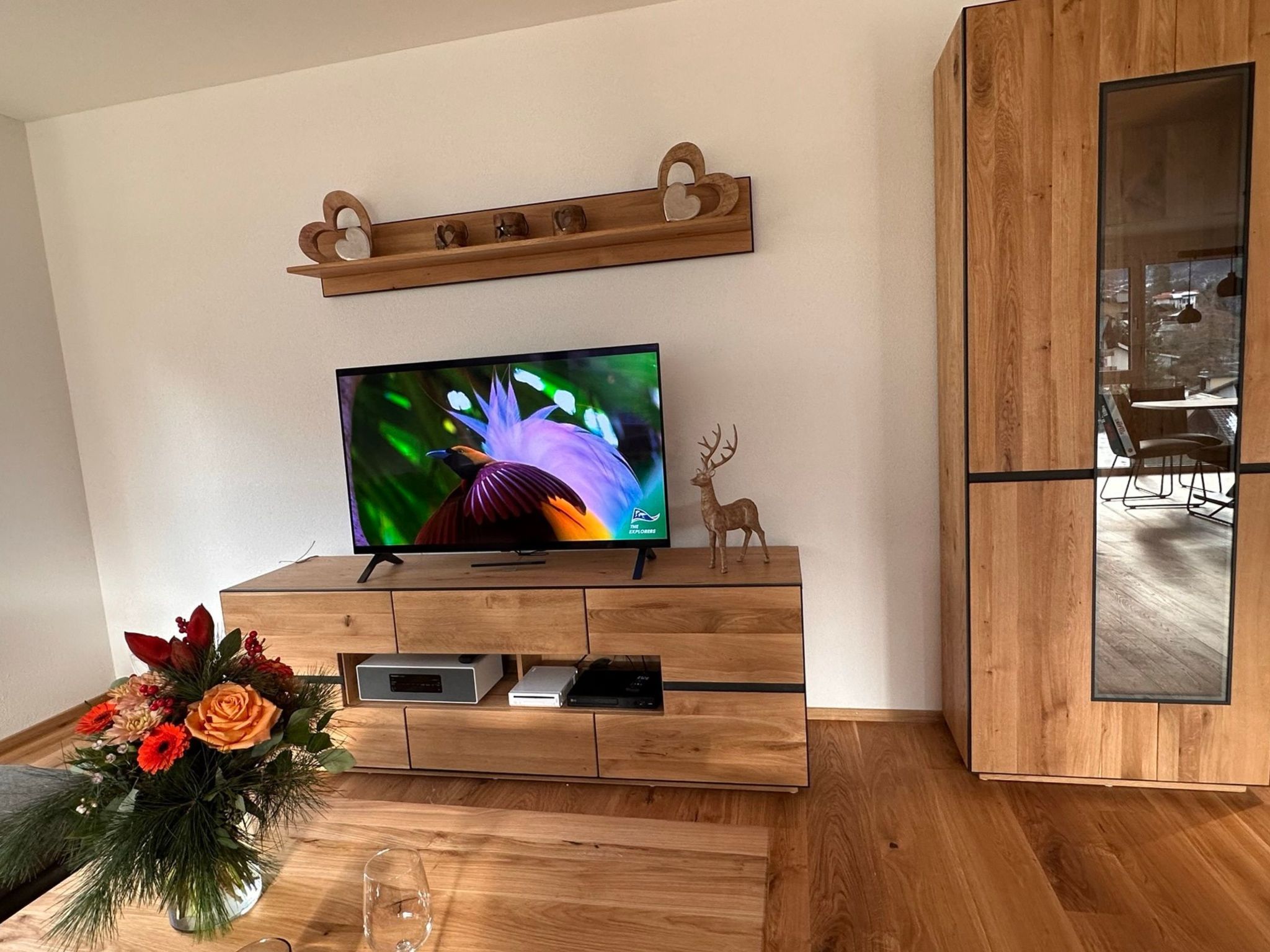 Eine Holzunterhaltungseinheit mit einem Flachbildfernseher, einem dekorativen Hirsch und einer Blumenkomposition.