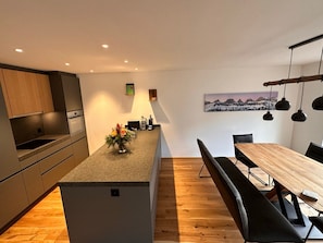 Eine moderne Küche mit einer zentralen Kochinsel, Holzboden und einer Essecke mit einem langen Tisch und Bänken.