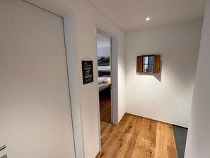 Ein Flur mit Holzboden, einem Bett im Hintergrund und einem kleinen Fenster mit Blick.
