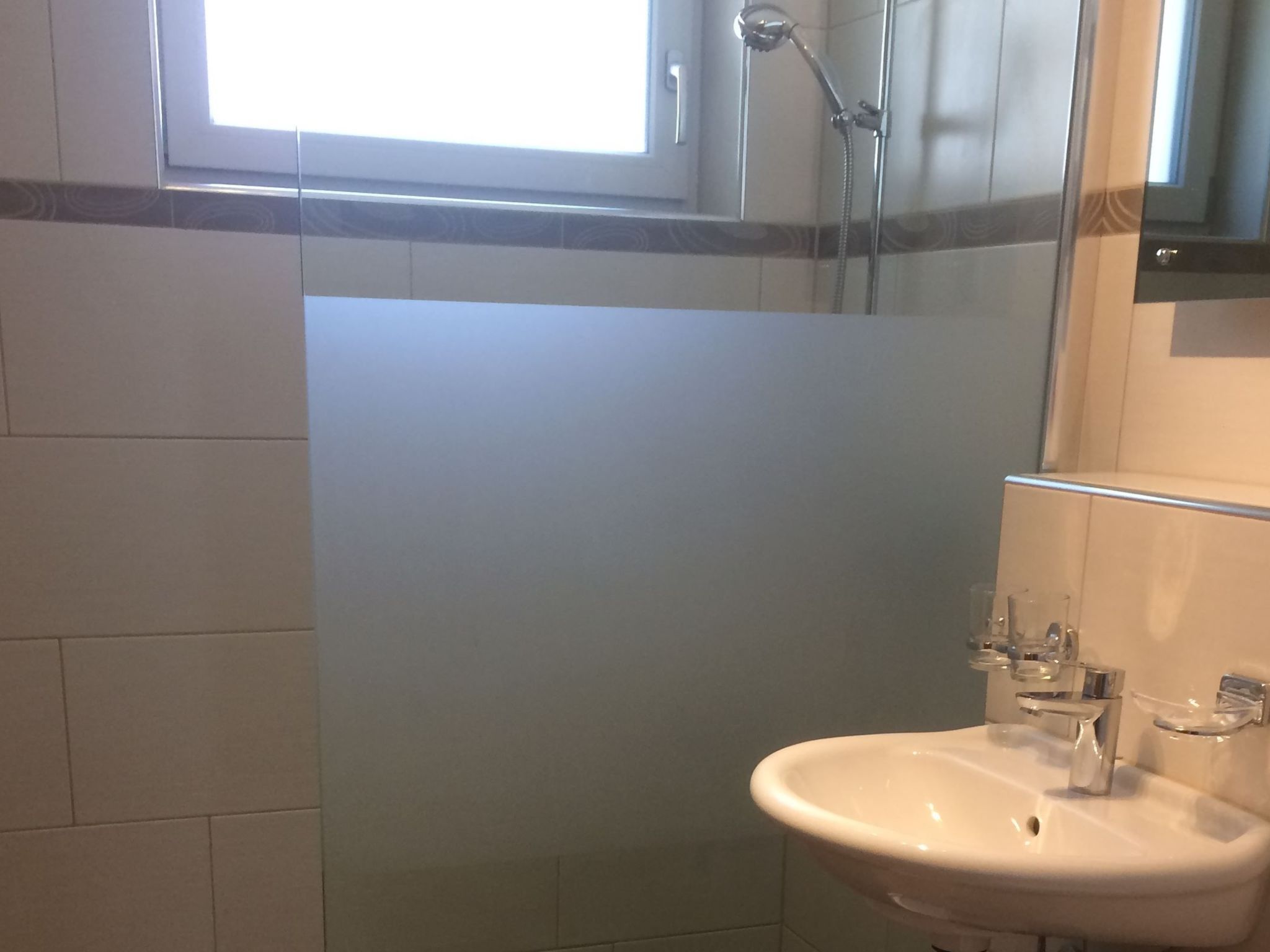 Un baño con cabina de ducha de vidrio, un lavabo blanco y un espejo.