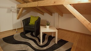 A room with a sloped ceiling, a black chair with a green pillow, a small white table with a plant, and a black and white rug. - Casa Riposo, (Flumserberg Tannenheim), by Interhome (Flumserberg Tannenheim)