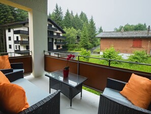 Ein Balkon mit Korbmöbeln, einem Glastisch und einem Blumentopf.