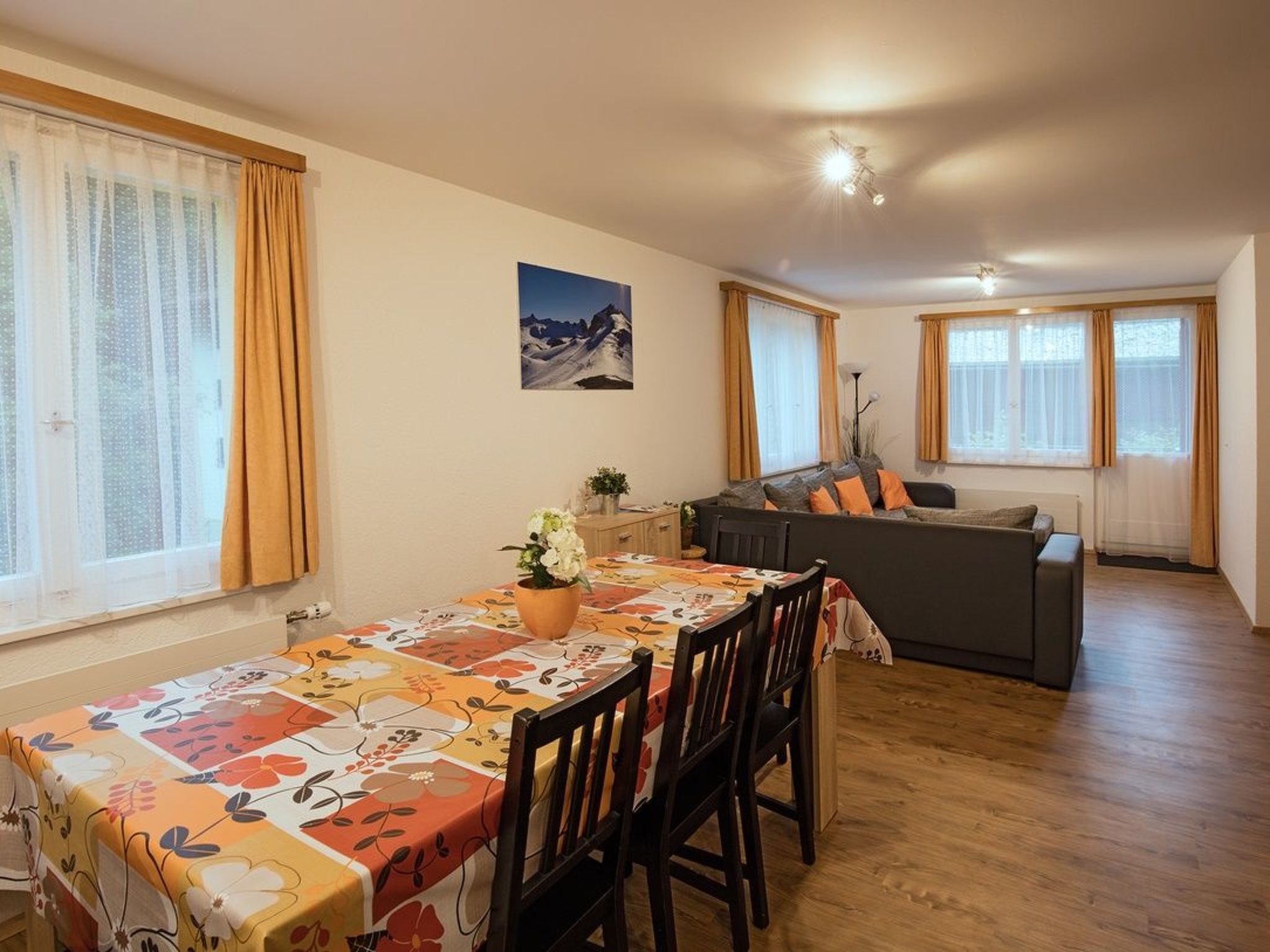 Un comedor con una mesa dispuesta para cuatro personas, un sofá y una zona de cocina al fondo.