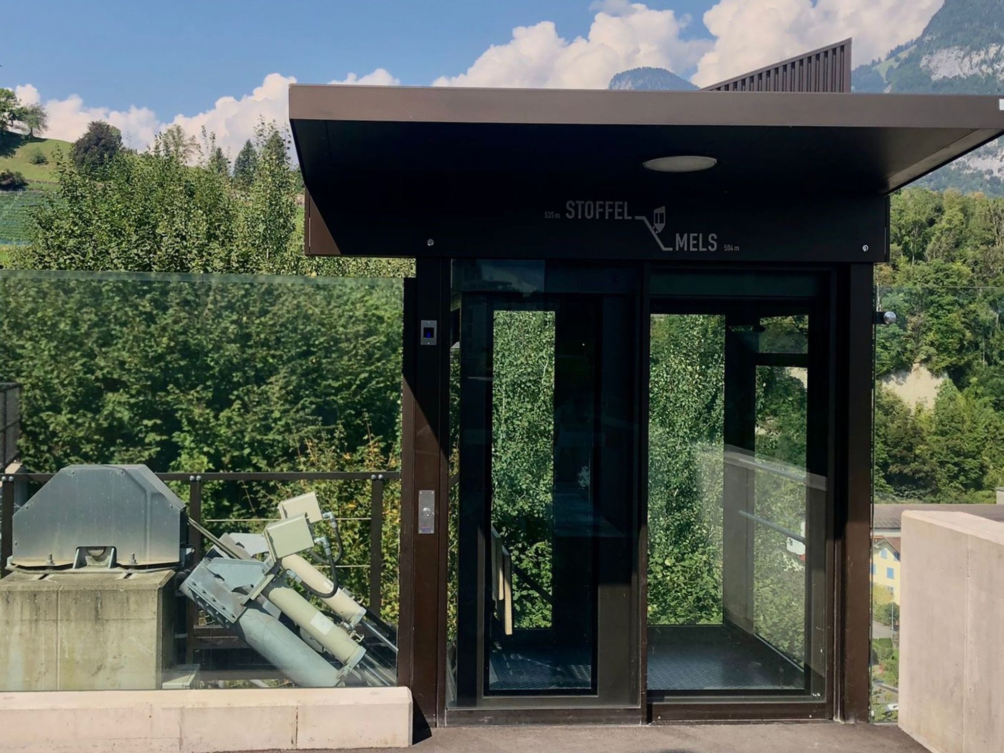 A modern building entrance with a glass door and a sign indicating 'STOFFEL MELS' at 535m elevation.