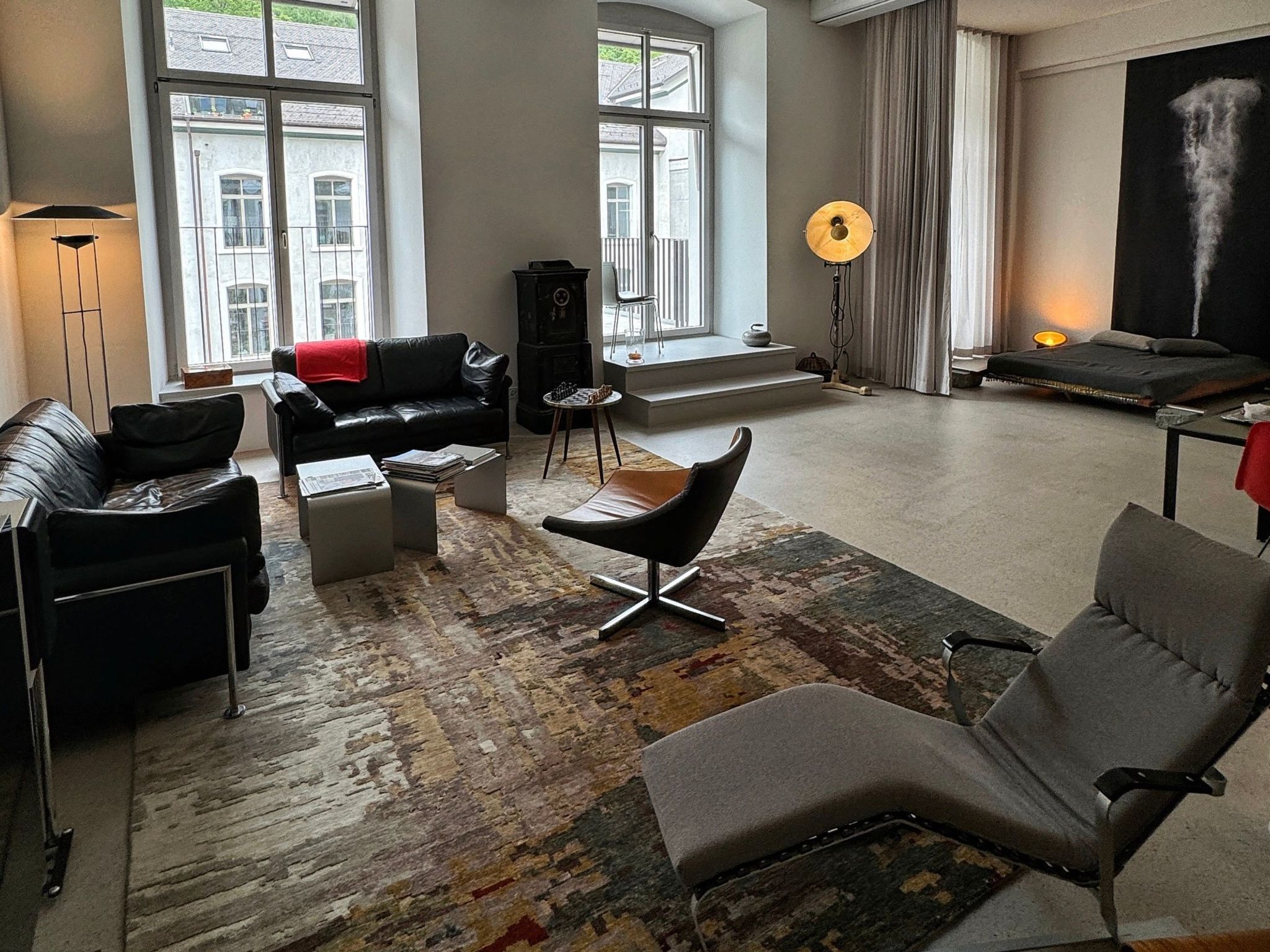 Una sala de estar moderna con un sofá, un sillón y una mesa de centro. Hay un ventanal con vistas a edificios.