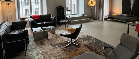 Una sala de estar moderna con un sofá, un sillón y una mesa de centro. Hay un ventanal con vistas a edificios.