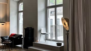 A modern living room with a large window, a black cabinet, a white chair, and a floor lamp.