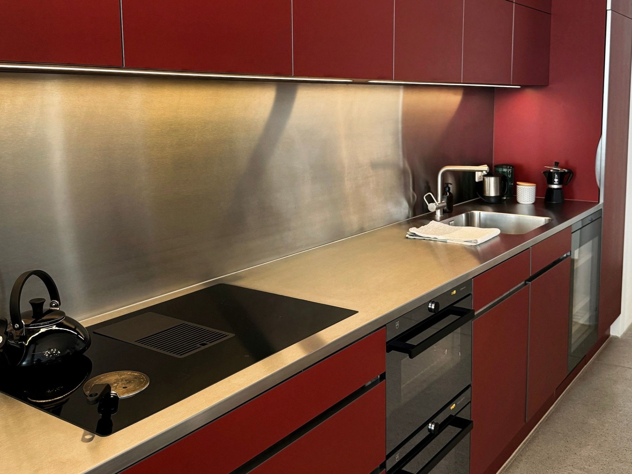 A modern kitchen with stainless steel appliances, red cabinetry, and a black kettle on the counter.