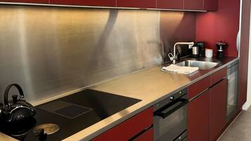 A modern kitchen with stainless steel appliances, red cabinetry, and a black kettle on the counter.