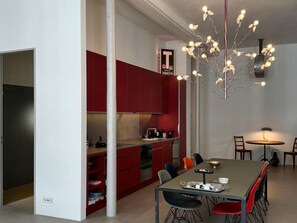 A modern kitchen with red cabinets, a dining area with a table and chairs, and a unique light fixture. - Design Loft - Herrschaftlich, (Mels), by Interhome (Mels)