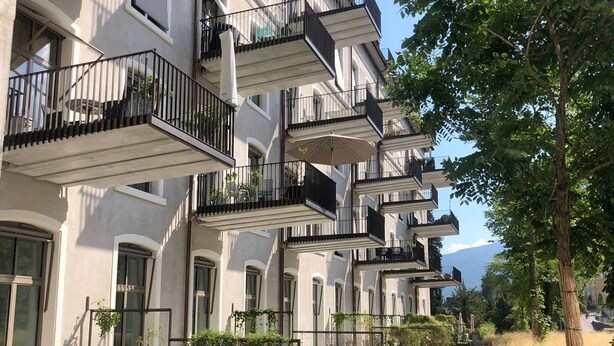 Una hilera de edificios modernos de varios pisos con balcones, mobiliario exterior y áreas verdes.