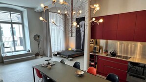 Una cocina moderna con gabinetes rojos, una zona de comedor con una mesa larga y sillas, y una lámpara de techo original.
