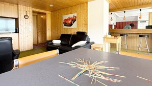 A modern interior with a wooden ceiling, a black leather sofa, a dining table with chairs, and a kitchen area. - Haus DOMO, (Flumserberg Tannenboden), by Interhome (Mols)