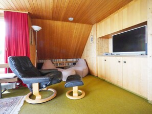 A cozy room with a wooden ceiling, a television, a bookshelf, and a red curtain.