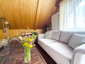Un dormitorio tipo loft acogedor con techo de madera, un sofá, una mesa de centro con un jarrón de flores y una estantería.