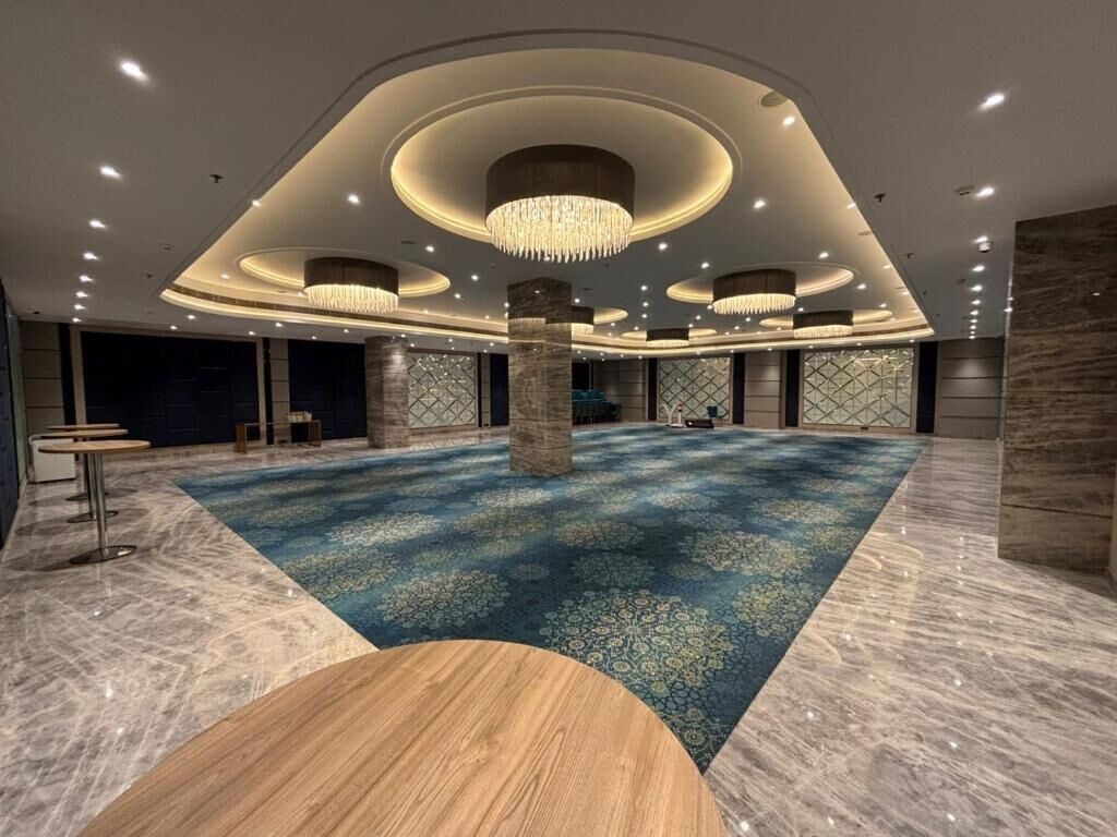 Un amplio espacio interior con piso alfombrado, varios arreglos de asientos y una columna central.