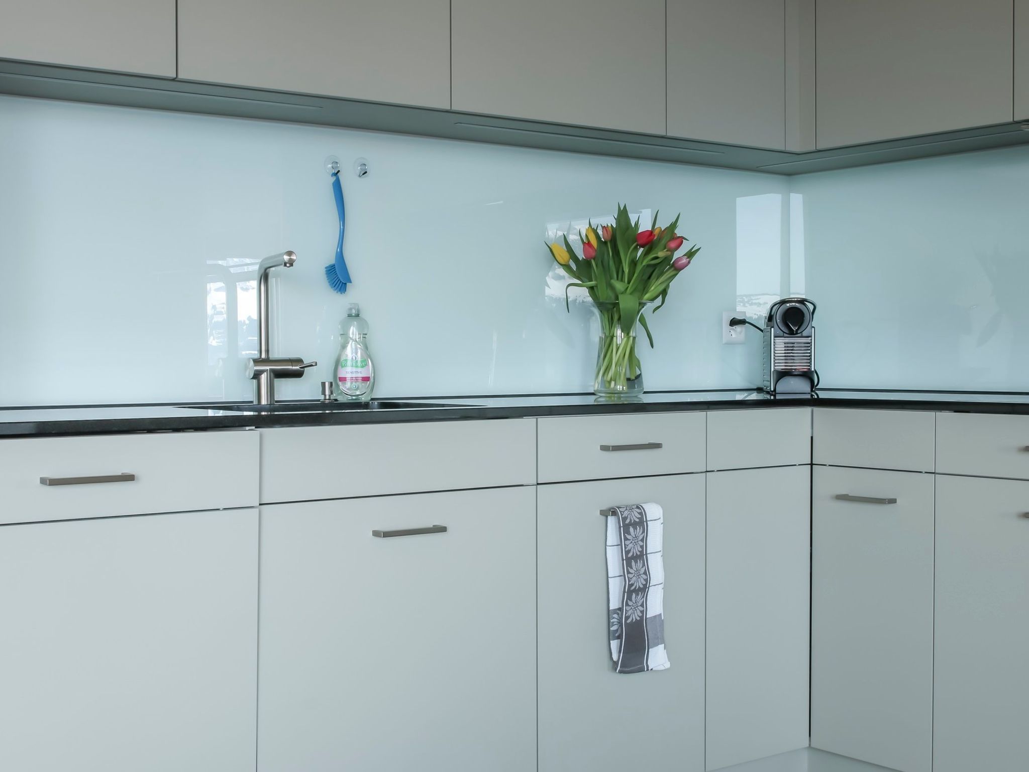 Une cuisine moderne avec un pare-feu en verre, un robinet en acier inoxydable et un vase de tulipes posé sur le plan de travail.